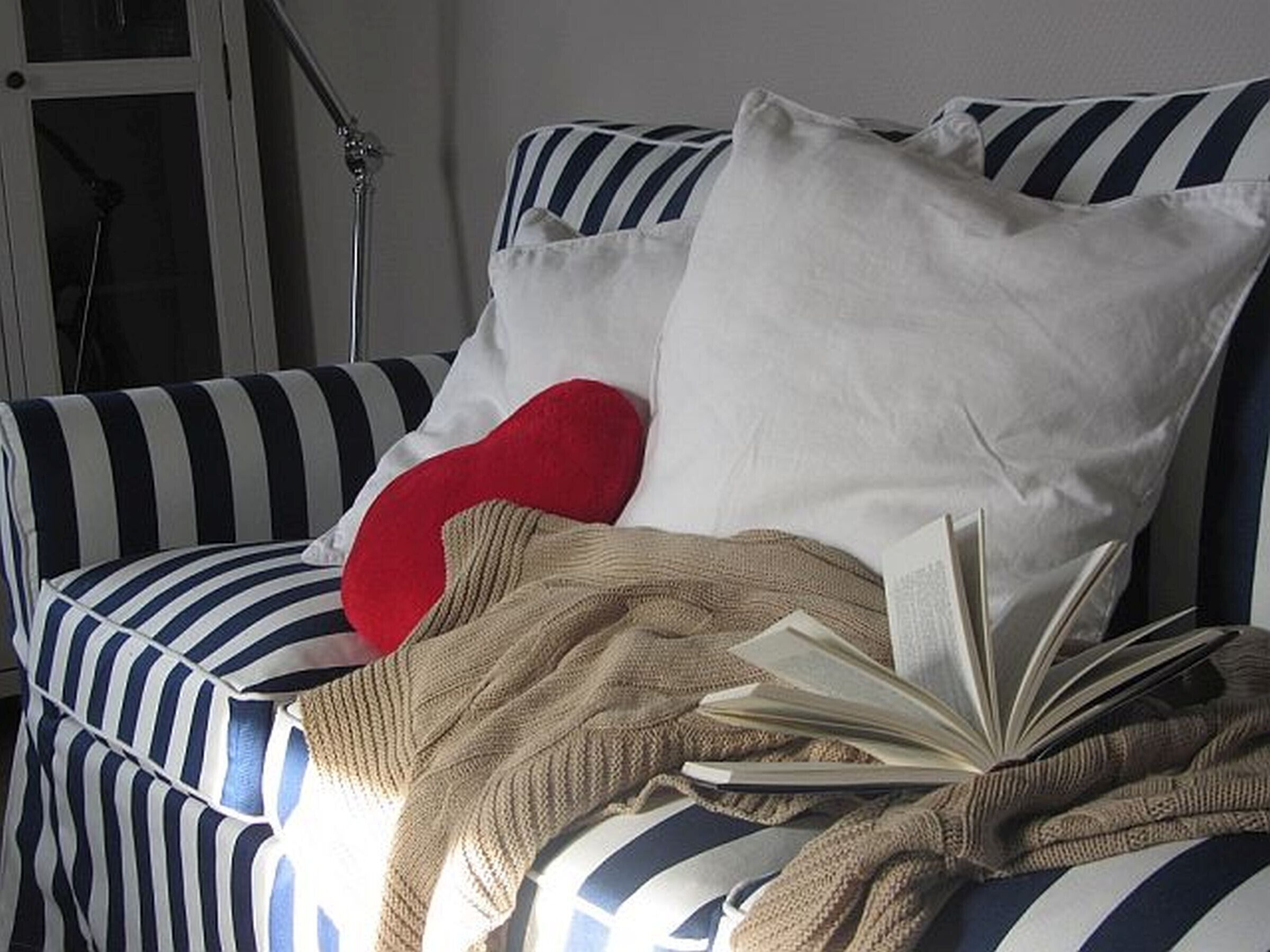 Un canapé à rayures, agrémenté d’un coussin rouge, d’un coussin blanc et d’une couverture beige.