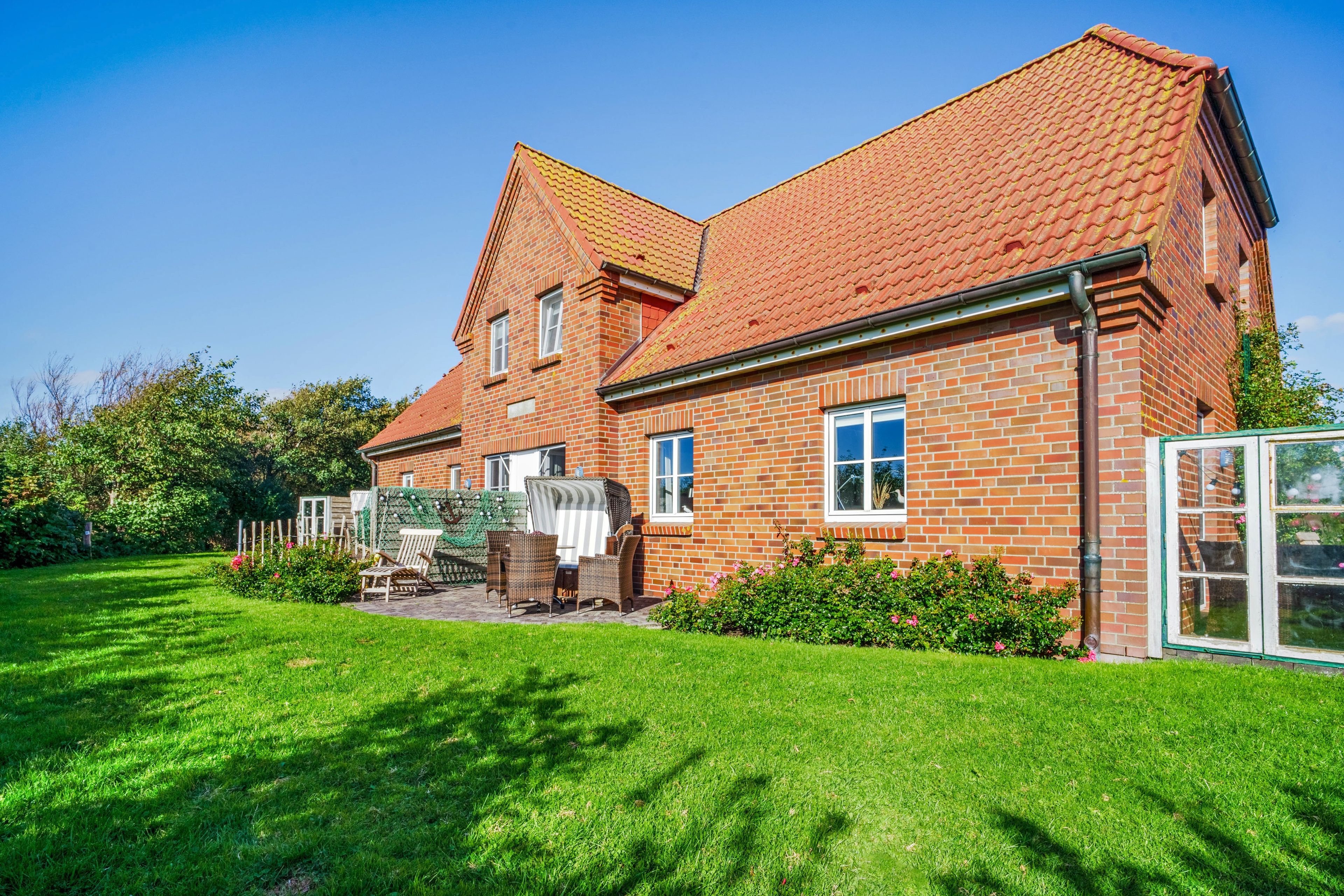 A two-story brick house with a sloped roof, a patio with outdoor furniture, and a well-maintained garden.