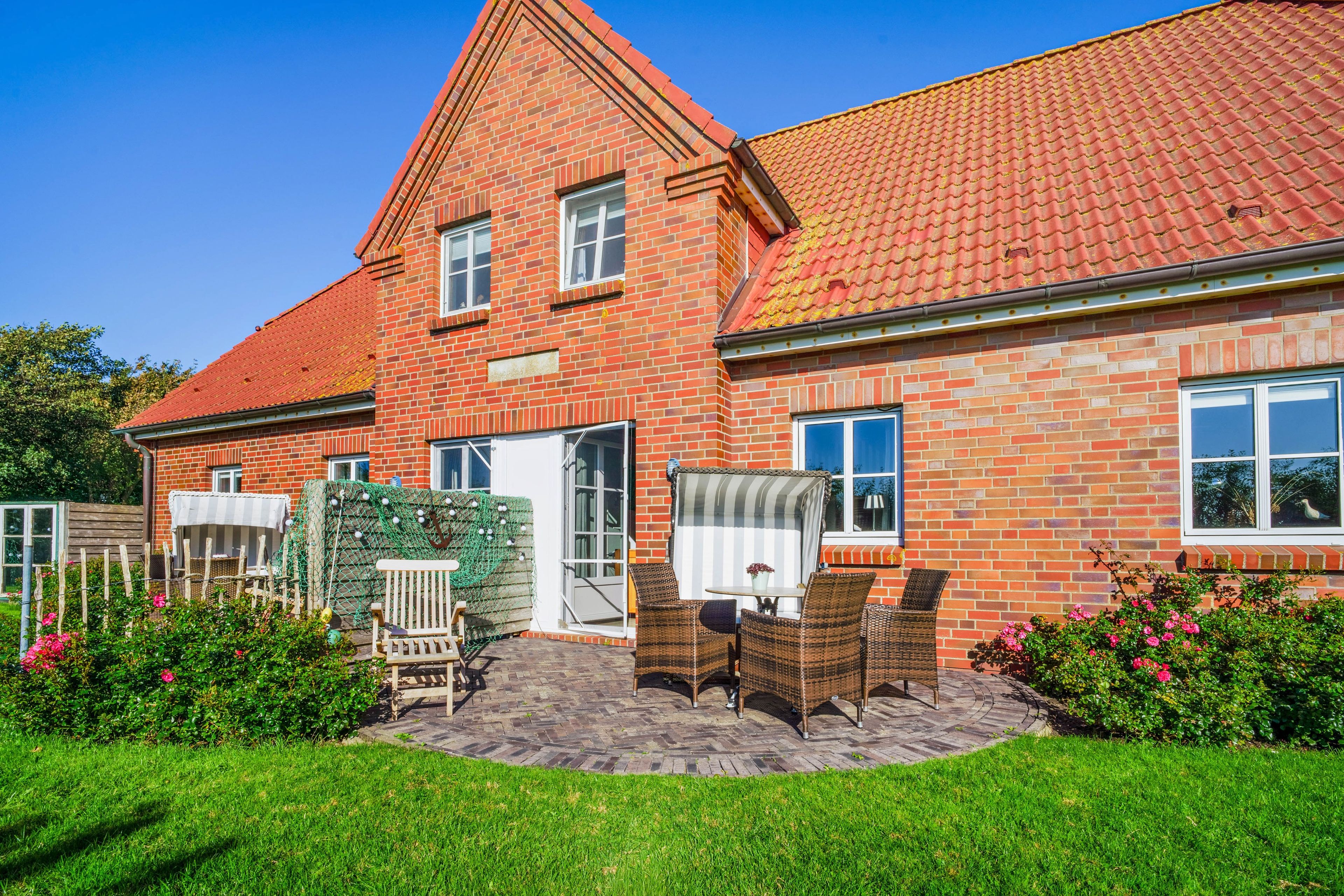 A two-story brick house with a red-tiled roof, a front porch with wicker furniture, and a well-maintained garden.