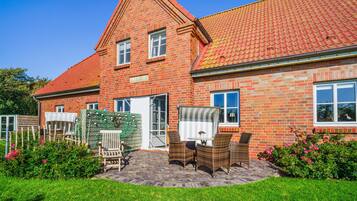 A two-story brick house with a red-tiled roof, a front porch with wicker furniture, and a well-maintained garden.