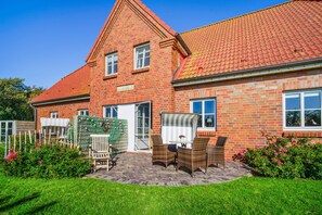 A two-story brick house with a red-tiled roof, a front porch with wicker furniture, and a well-maintained garden. - Apartment 'Inselliebe' with Private Terrace, Shared Garden & Wi-Fi (Pellworm)