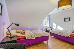 Un dormitorio con dos camas, un escritorio con lámpara, una silla de mimbre y una ventana con cortinas.