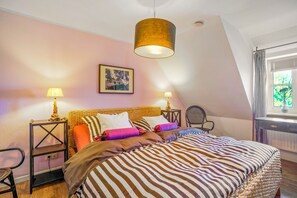 A bedroom with a bed, two bedside tables, a chair, a hanging lamp, and a window with curtains. - Apartment 'Inselliebe' with Private Terrace, Shared Garden & Wi-Fi (Pellworm)