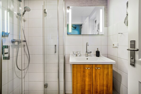 A bathroom with a glass shower enclosure, a wooden cabinet with a sink, and a mirror above the sink.