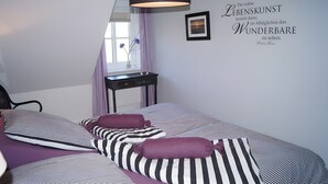 Ein Schlafzimmer mit Bett, Kissen, Schreibtisch, Lampe und einer Wand mit einem Zitat.