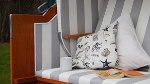 A striped lounge chair with a cushion, a white mug, and a book. - Apartment 'Sonnenkuss' with Private Terrace, Shared Garden & Wi-Fi (Pellworm)