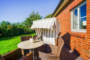 Een terras met rieten meubels en een tafel, naast een gebouw met bakstenen muren en een raam.