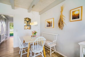 A dining area with a white table, chairs, and a wall-mounted light fixture. - Apartment 'Sonnenkuss' with Private Terrace, Shared Garden & Wi-Fi (Pellworm)