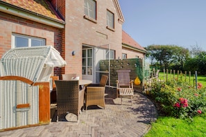A patio with wicker furniture, a brick house, and a garden with roses. - Apartment 'Sonnenkuss' with Private Terrace, Shared Garden & Wi-Fi (Pellworm)