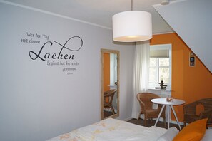 Ein Schlafzimmer mit einem Bett, einem Sessel, einem kleinen Tisch, einem Spiegel und einer Wand mit einem Zitat.