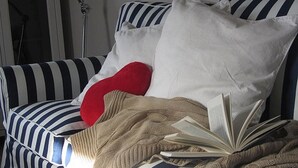 A striped sofa with a red pillow, a white pillow, and a beige blanket. - Apartment 'Windsbraut' with Private Terrace, Shared Garden & Wi-Fi (Pellworm)
