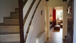 A staircase leading to a room with a radiator, a red curtain, and a wicker chair. - Apartment 'Windsbraut' with Private Terrace, Shared Garden & Wi-Fi (Pellworm)