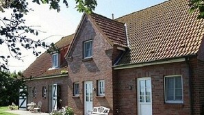 A two-story brick house with a tiled roof, a front porch with a bench, and a small garden area. - Apartment 'Windsbraut' with Private Terrace, Shared Garden & Wi-Fi (Pellworm)