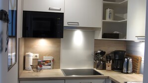A modern kitchen with a microwave, oven, and coffee maker. - Apartment 'Windsbraut' with Private Terrace, Shared Garden & Wi-Fi (Pellworm)