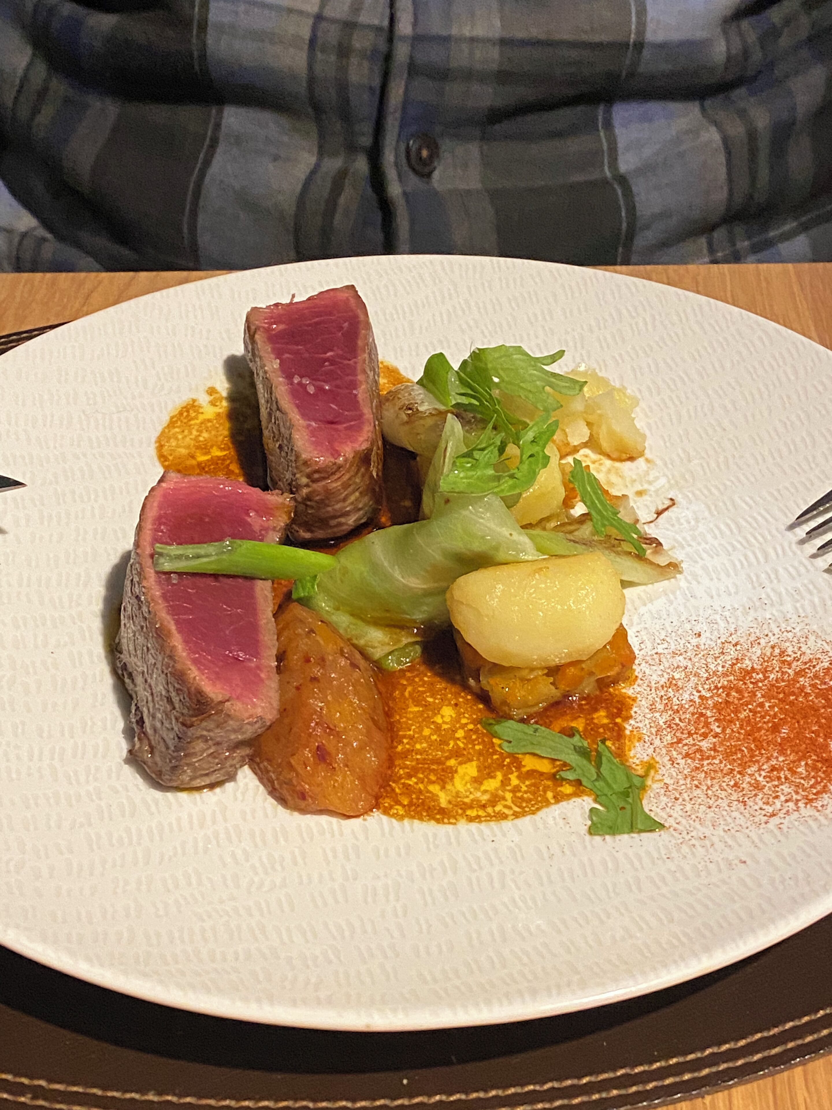 A plate of food with steak, potatoes, and greens on a paper plate.