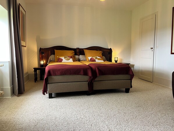 Una cama doble con cabecera de madera, dos mesitas de noche con lámparas, suelo alfombrado y una puerta blanca.