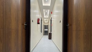 A long, narrow hallway with wooden doors on either side and a tiled floor. - Hotel Kalindi kunj (Mathura)