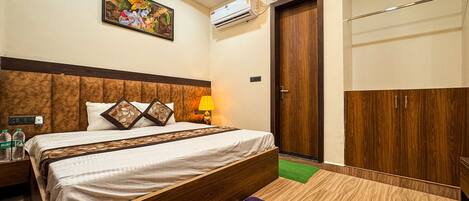 A hotel room with a bed, a nightstand, a lamp, an air conditioning unit, a wardrobe, and a wall-mounted picture.