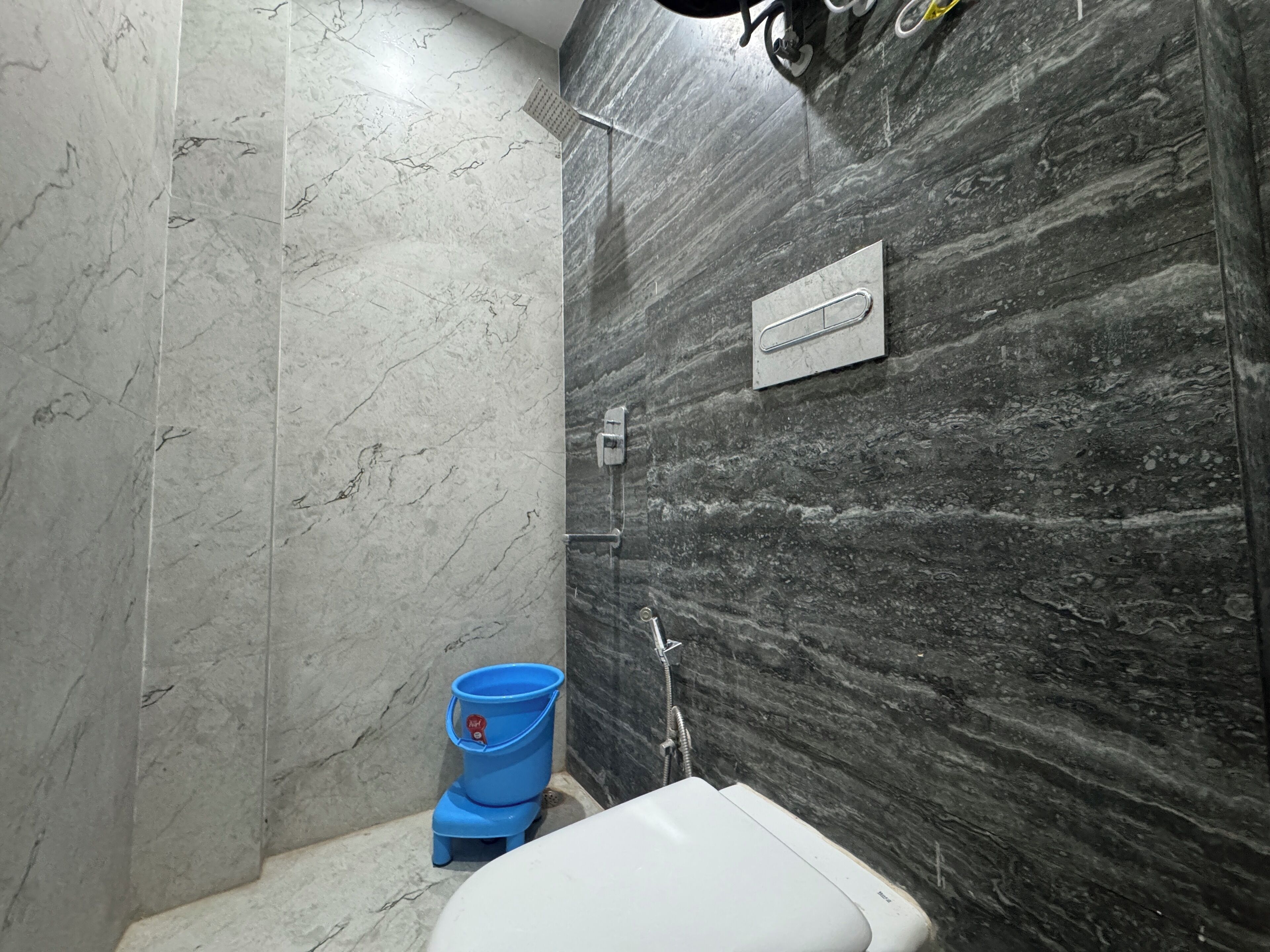 A bathroom with a toilet, a blue bucket, and a shower area.