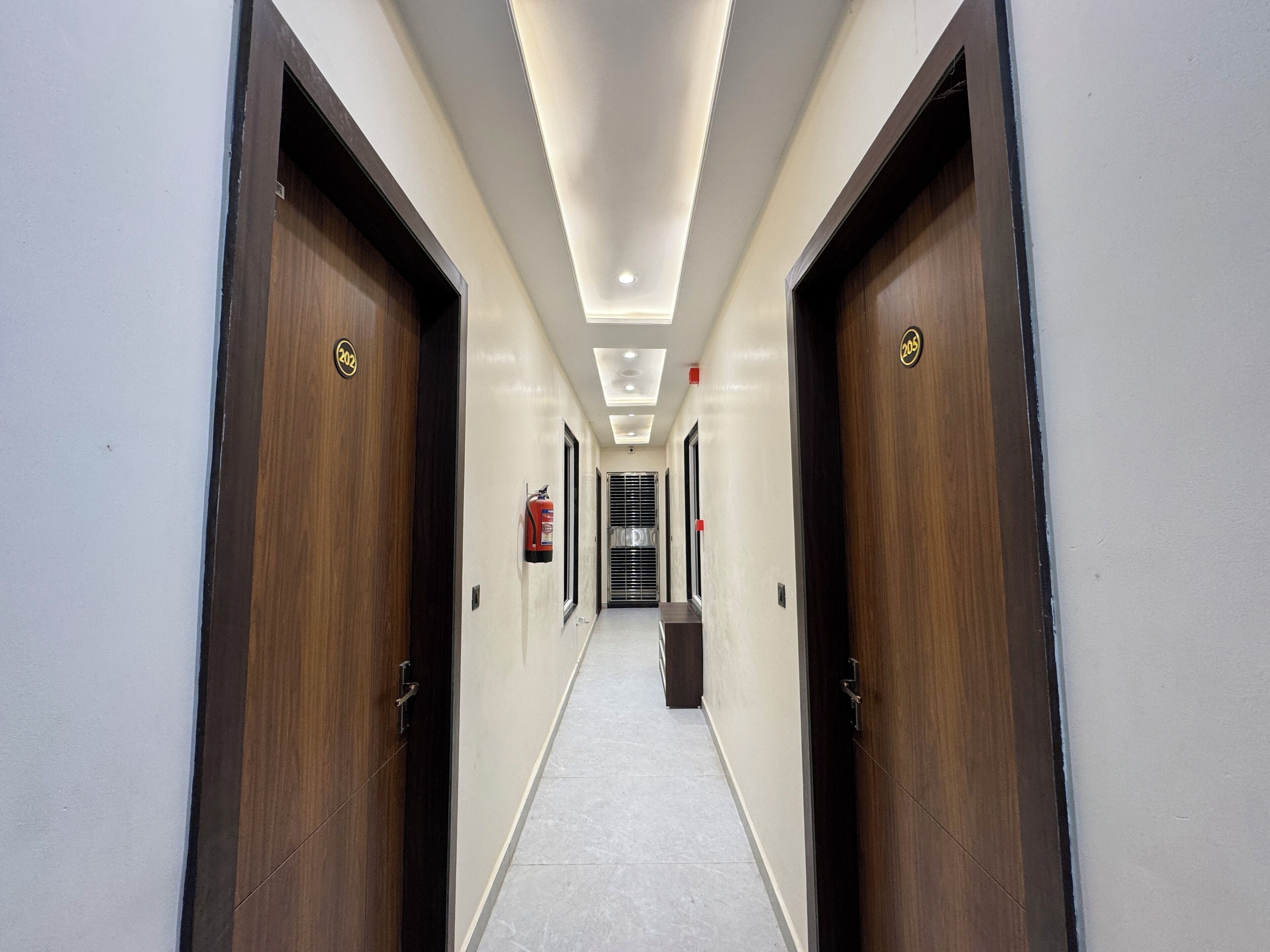 A hallway with wooden doors, a fire extinguisher, and a trash bin.