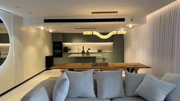 Een modern interieur met een houten eettafel, een bank met kussens en een keuken in de achtergrond.