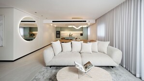 A modern living room with a sofa, a coffee table, and a dining area in the background. - Artemis (Tiberias)