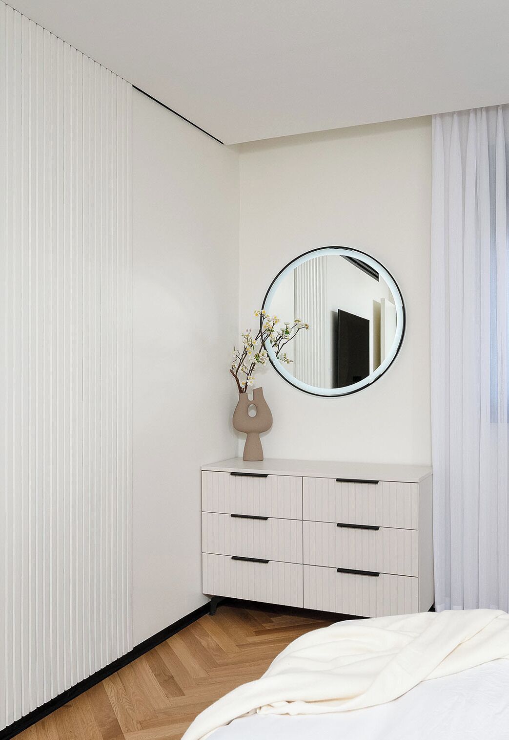 A bedroom with a bed, a dresser, a mirror, and a vase with flowers.