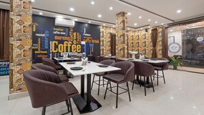 A modern cafe with tables and chairs, a word cloud on the wall, and a logo on the glass door. - Treebo Sri Krishna Palace (Bhubaneshwar)