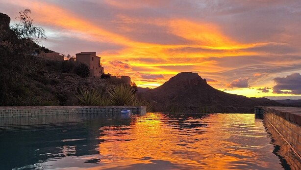 A serene sunset over a calm pool with a stone wall and a building on the left. - Cozy villa with infinity pool in the mountains of Sierra Cabrera (TURRE)