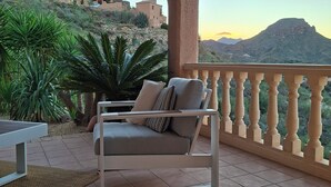 A terrace with a cushioned seating area, a view of a mountainous landscape, and a stone wall. - Cozy villa with infinity pool in the mountains of Sierra Cabrera (TURRE)