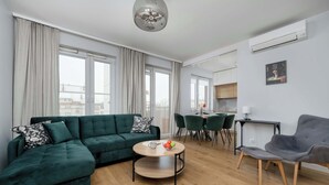 Una sala de estar moderna con un sofá modular, una mesa de centro redonda y un sillón gris. Se aprecia un comedor con mesa y sillas, y una cocina al fondo.