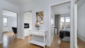 Un apartamento moderno con una consola blanca, un cuadro y una cama con manta gris.