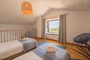 Ein Schlafzimmer mit zwei Betten, einem Fenster mit Vorhängen, einem blauen Stuhl und einer Pendelleuchte.