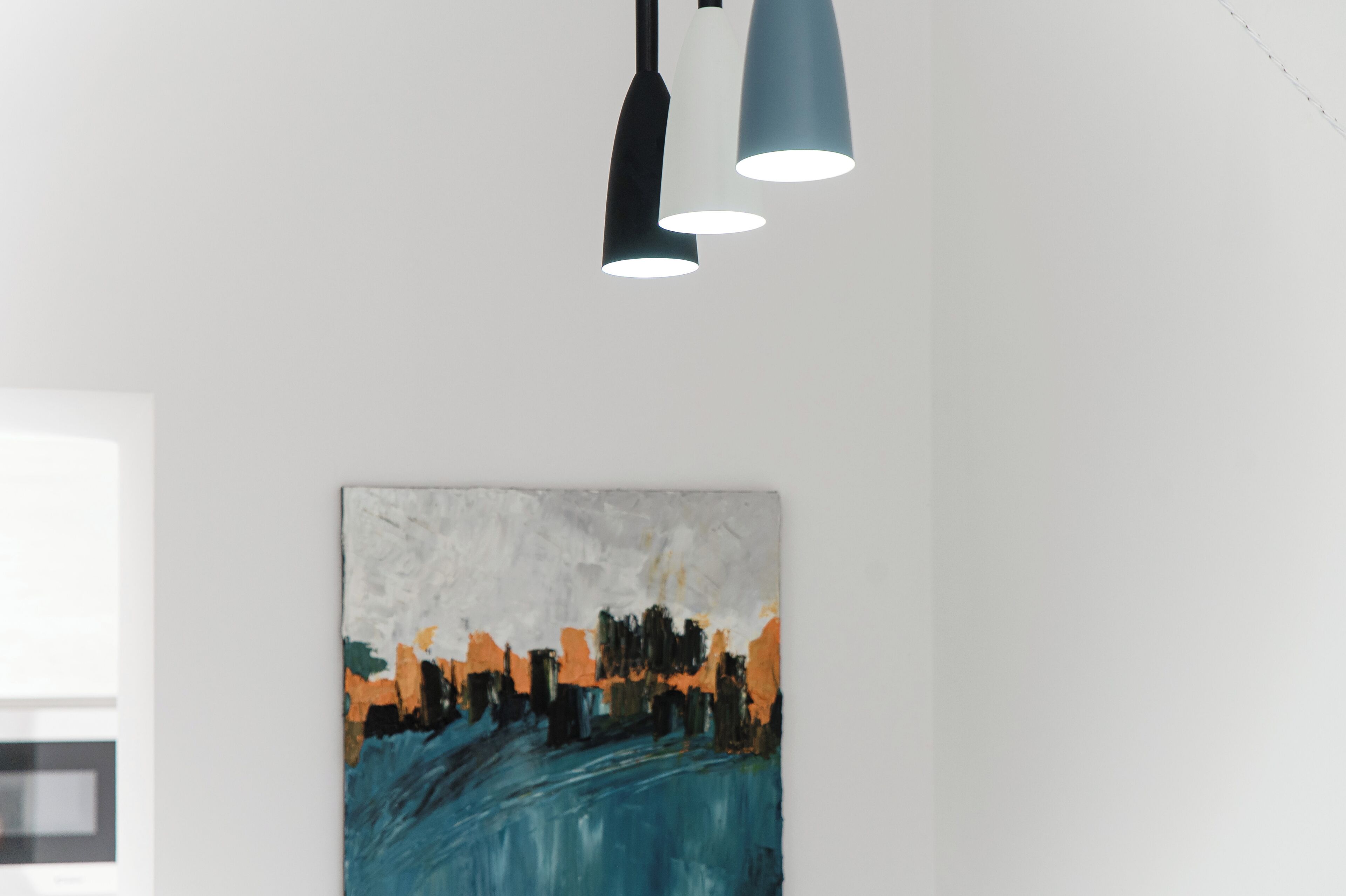 Een modern interieur met een minimalistisch plafondontwerp, een abstract kunstwerk aan de muur, en een raam dat natuurlijk licht binnenlaat.