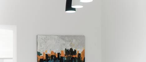Een modern interieur met een minimalistisch plafondontwerp, een abstract kunstwerk aan de muur, en een raam dat natuurlijk licht binnenlaat.