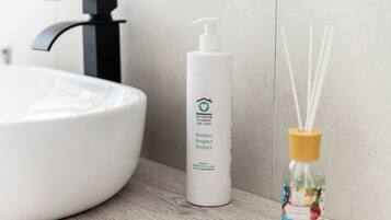 Un baño con un lavamanos blanco, una botella blanca de limpiador orgánico para manos y rostro, y un difusor de aroma de juncos.