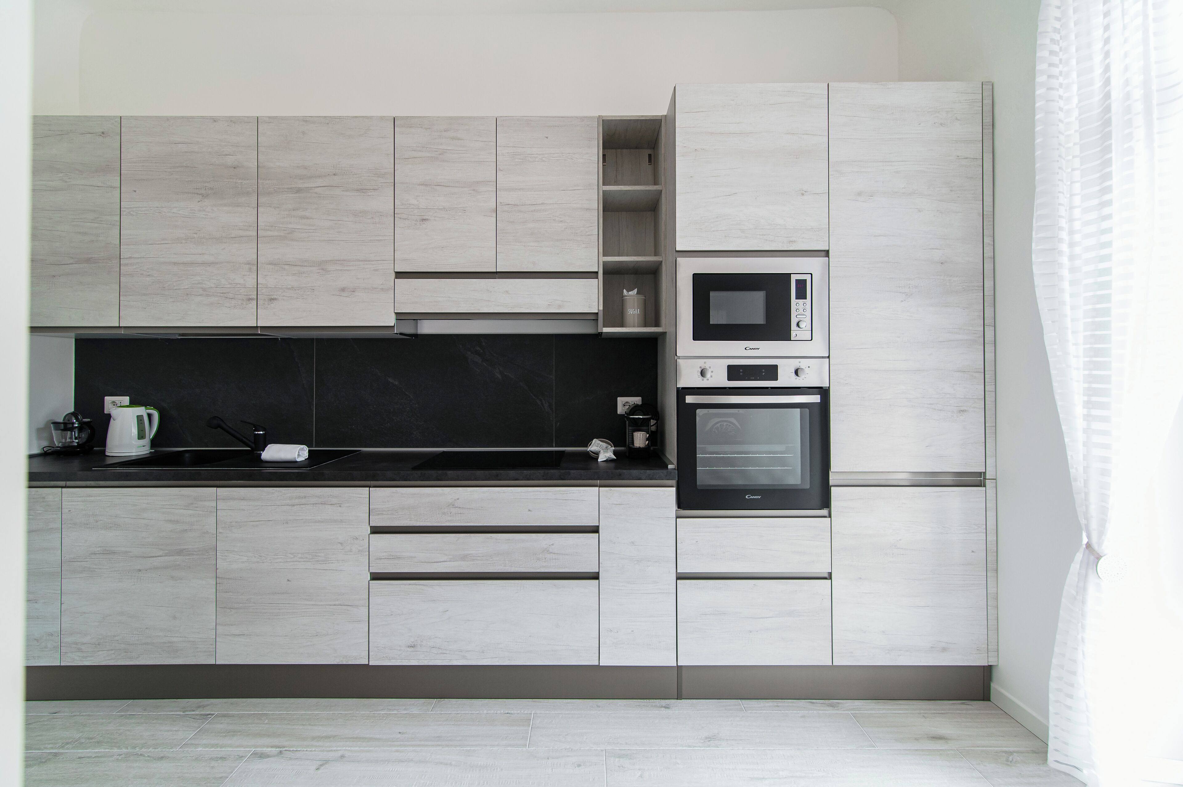 Una cocina moderna con armarios de madera clara, encimera negra, microondas integrado y horno.