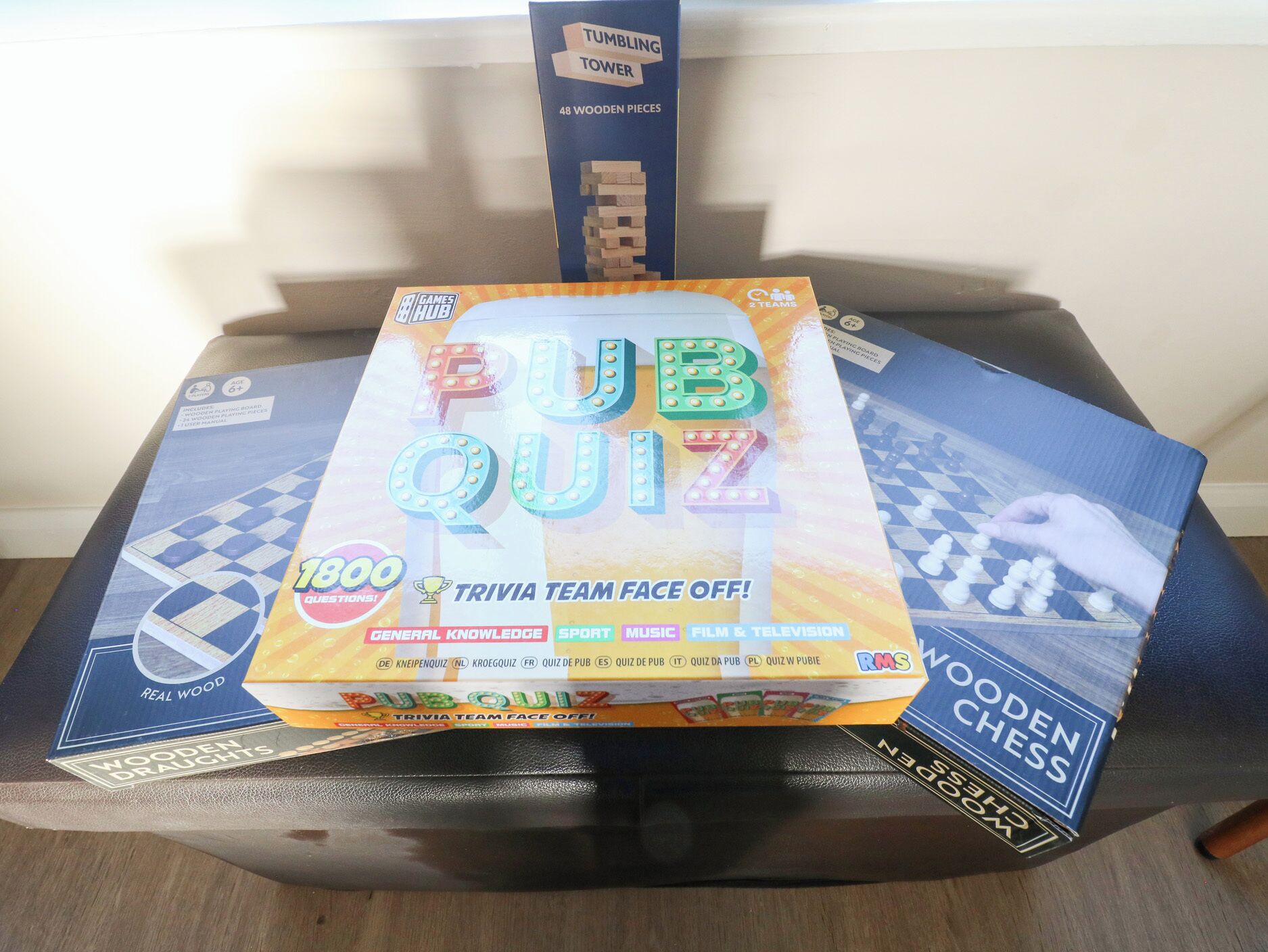 Una pila di giochi da tavolo, tra cui PUB QUIZ, TUMBLING TOWER e scacchi in legno, su un tavolo.