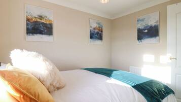 A bedroom with a bed, a fluffy white pillow, a teal blanket, and three abstract paintings on the wall.