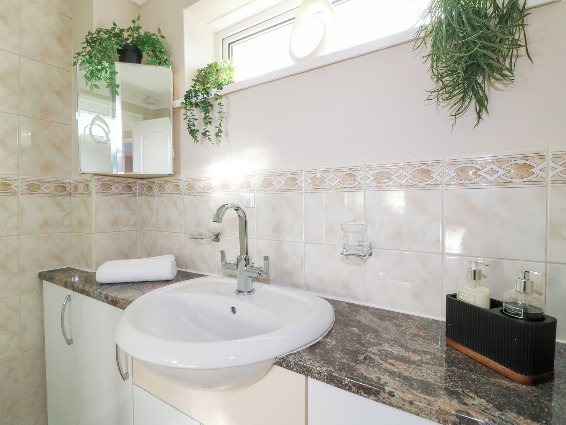 A bathroom with a white sink, a mirror, a towel, and decorative plants.
