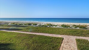 A coastal landscape with a paved walkway, grassy areas, and a sandy beach. - Gulf-Front Escape- 2BR Beachfront Condo by RVA (Longboat Key)