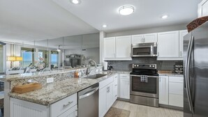 A modern kitchen with white cabinets, stainless steel appliances, and a granite countertop. - Gulf-Front Escape- 2BR Beachfront Condo by RVA (Longboat Key)