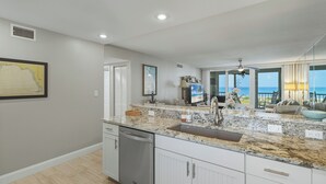 A modern kitchen with granite countertops, a dishwasher, and a large window overlooking the ocean. - Gulf-Front Escape- 2BR Beachfront Condo by RVA (Longboat Key)