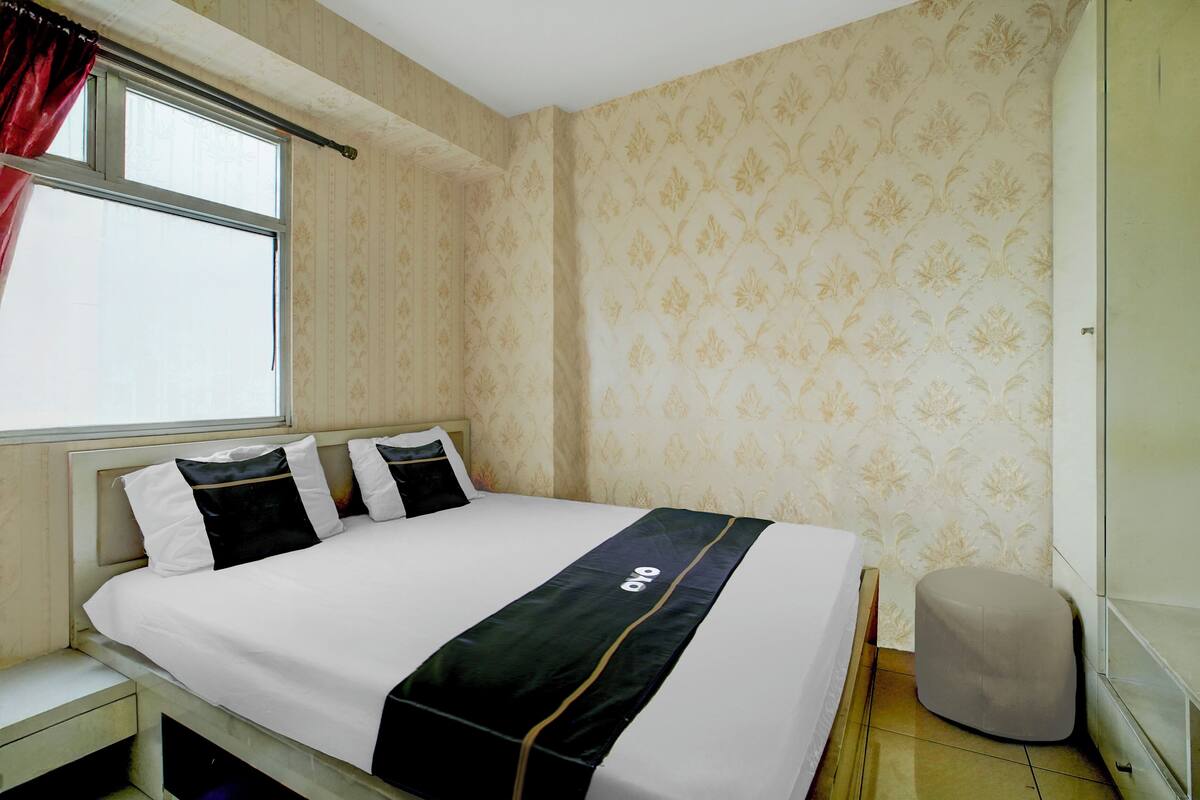 A neatly made bed with a black and white bedspread, a small bedside table, and a window with red curtains.