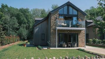 Une maison moderne à deux étages, dotée d’une façade en pierre, de grandes fenêtres et d’une pelouse bien entretenue.