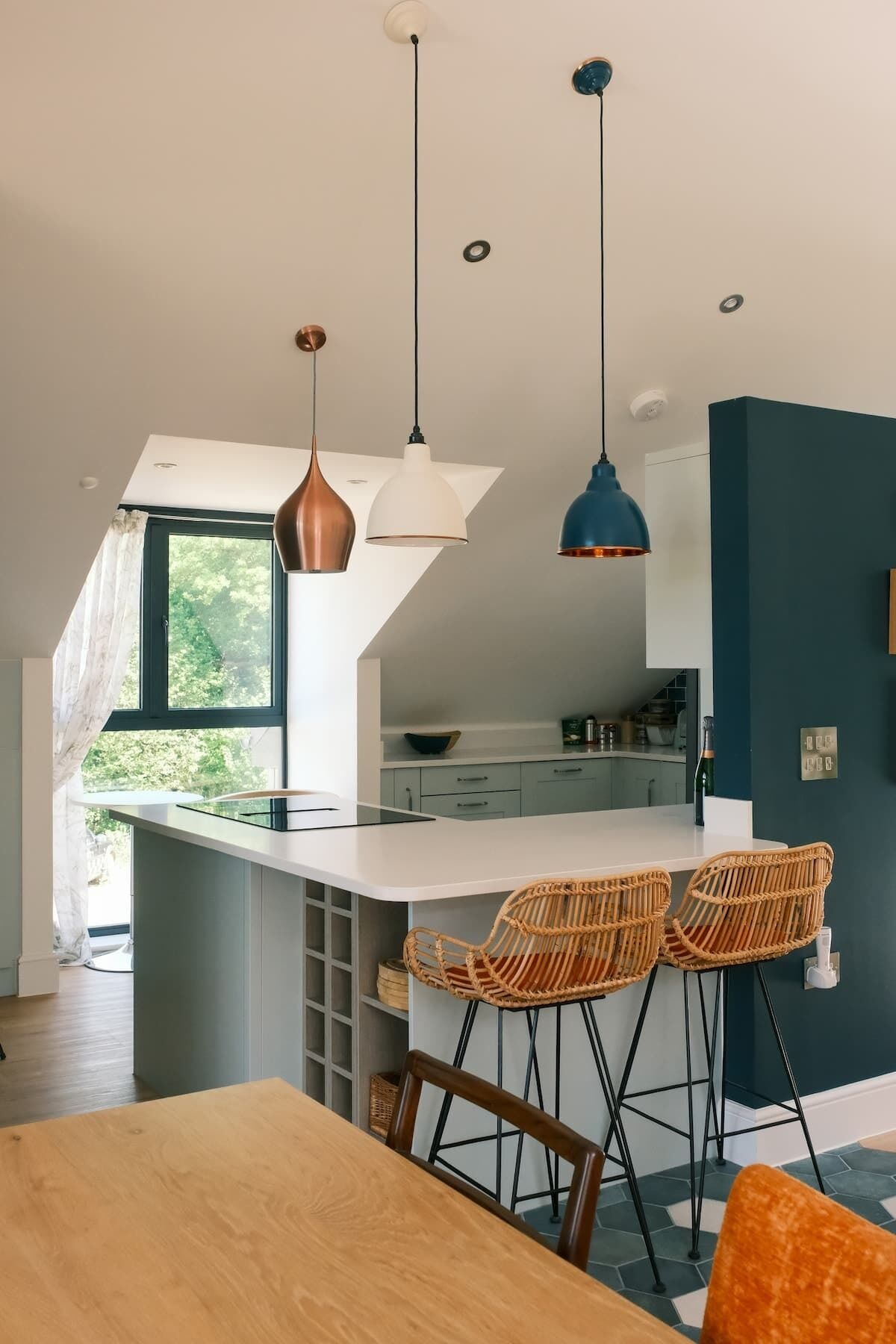 Une cuisine moderne dotée d’un îlot central, de luminaires suspendus et d’un coin repas avec des chaises en osier.