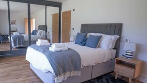 A modern bedroom with a large bed, a bedside table, a mirror, and a wardrobe.