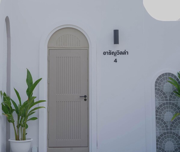 A white door with a small potted plant beside it, a tiled window with a decorative pattern, and a sign with a number. - Alan Pool Villa Bangsaen (Chonburi)