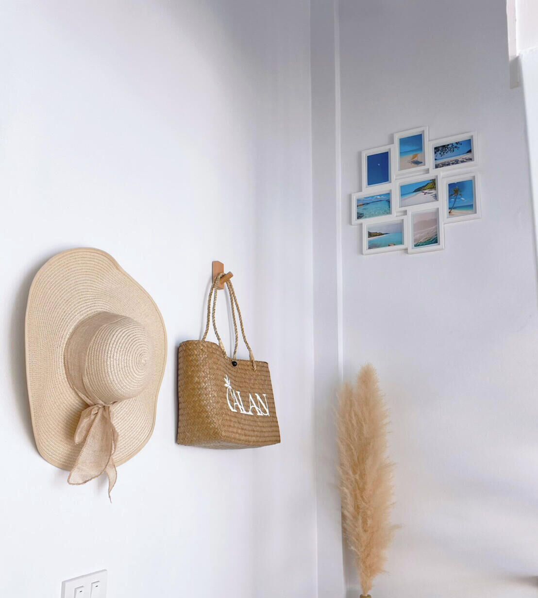 A wall with a straw hat and a woven bag hanging on hooks, and a series of small framed pictures depicting coastal scenes.