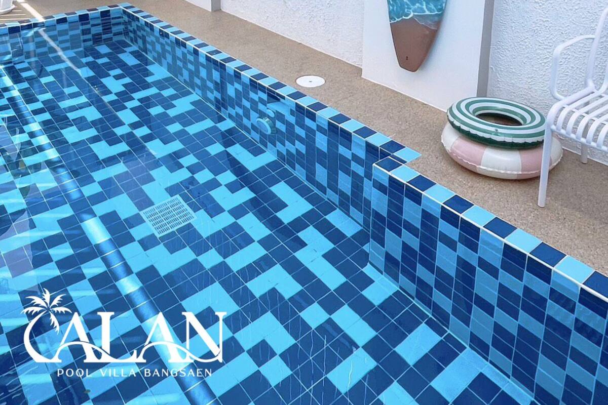 Una piscina con baldosas azules, una tabla de surf, un flotador salvavidas y una silla.